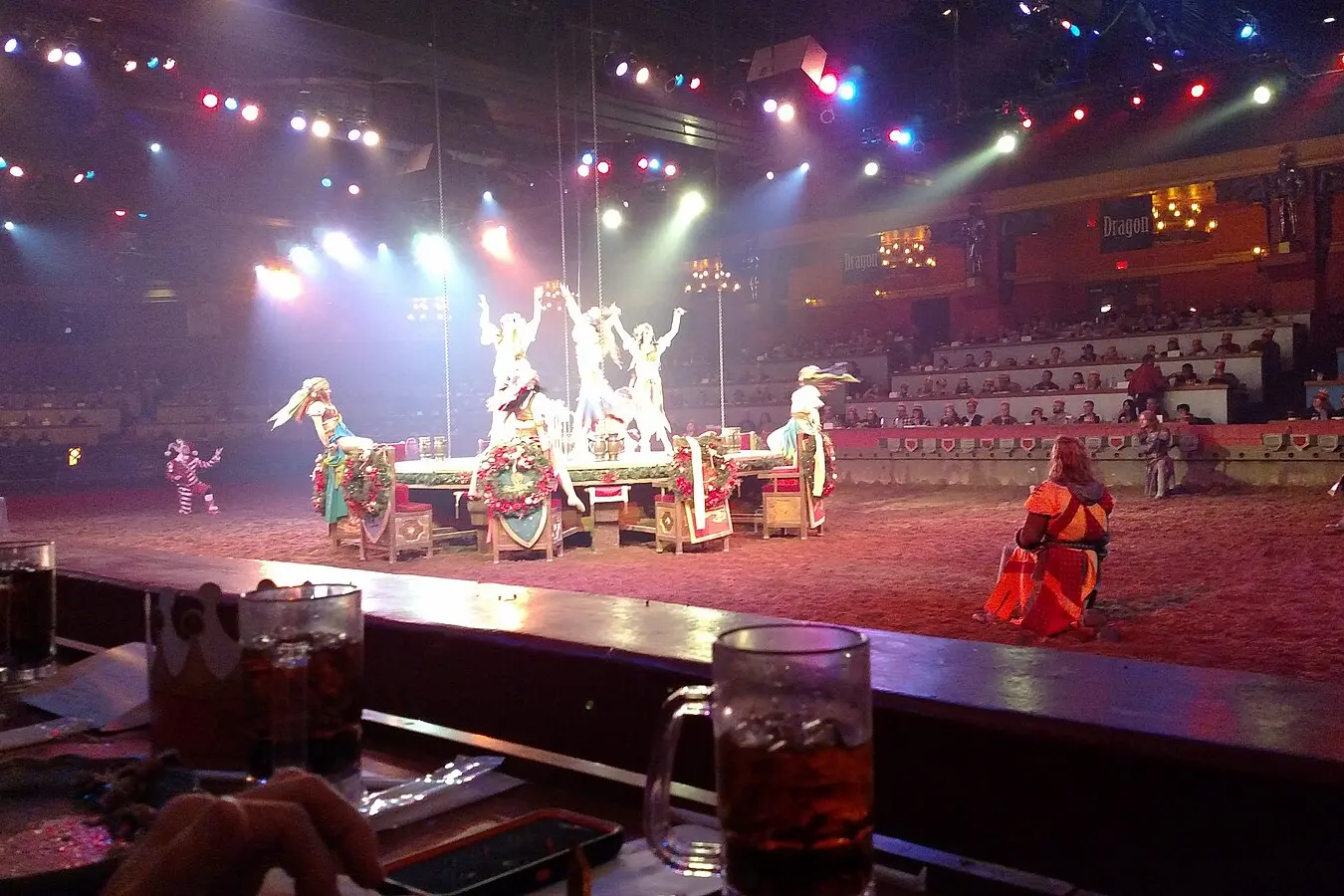 The Tournament of Kings dinner show in Las Vegas, featuring a lively medieval performance with costumed knights, dancers, and acrobats on a decorated stage. The arena-style seating surrounds the action as guests enjoy a themed feast while watching the live entertainment.