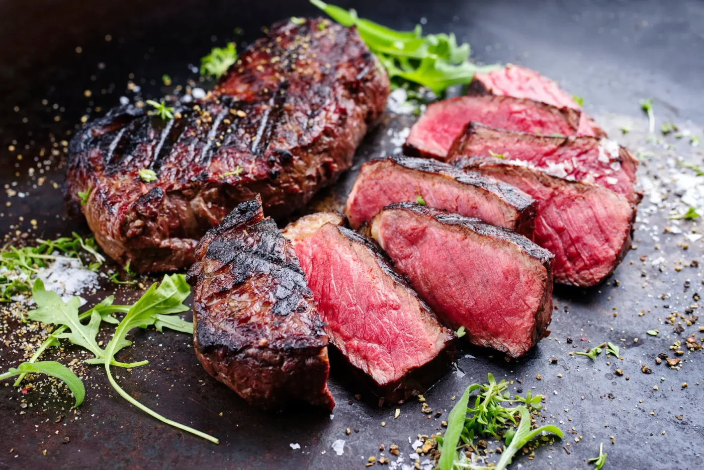 A perfectly grilled steak, sliced to reveal a juicy medium-rare center, served with fresh herbs and seasonings on a rustic slate plate for Las Vegas Restaurant Week.